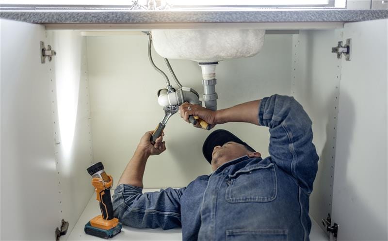 Plumber repairing pipes beneath a bathroom sink in Lodi